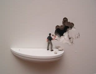 Digital photograph of an installation piece in which a white wall has been chipped away at revealing a deep hole. Slightly beneath the hold a white semi circle platform elevates a tiny figurine who holds a hammer in its hand. The figurine is assumed responsible for the several chips and deep cuts into the wall