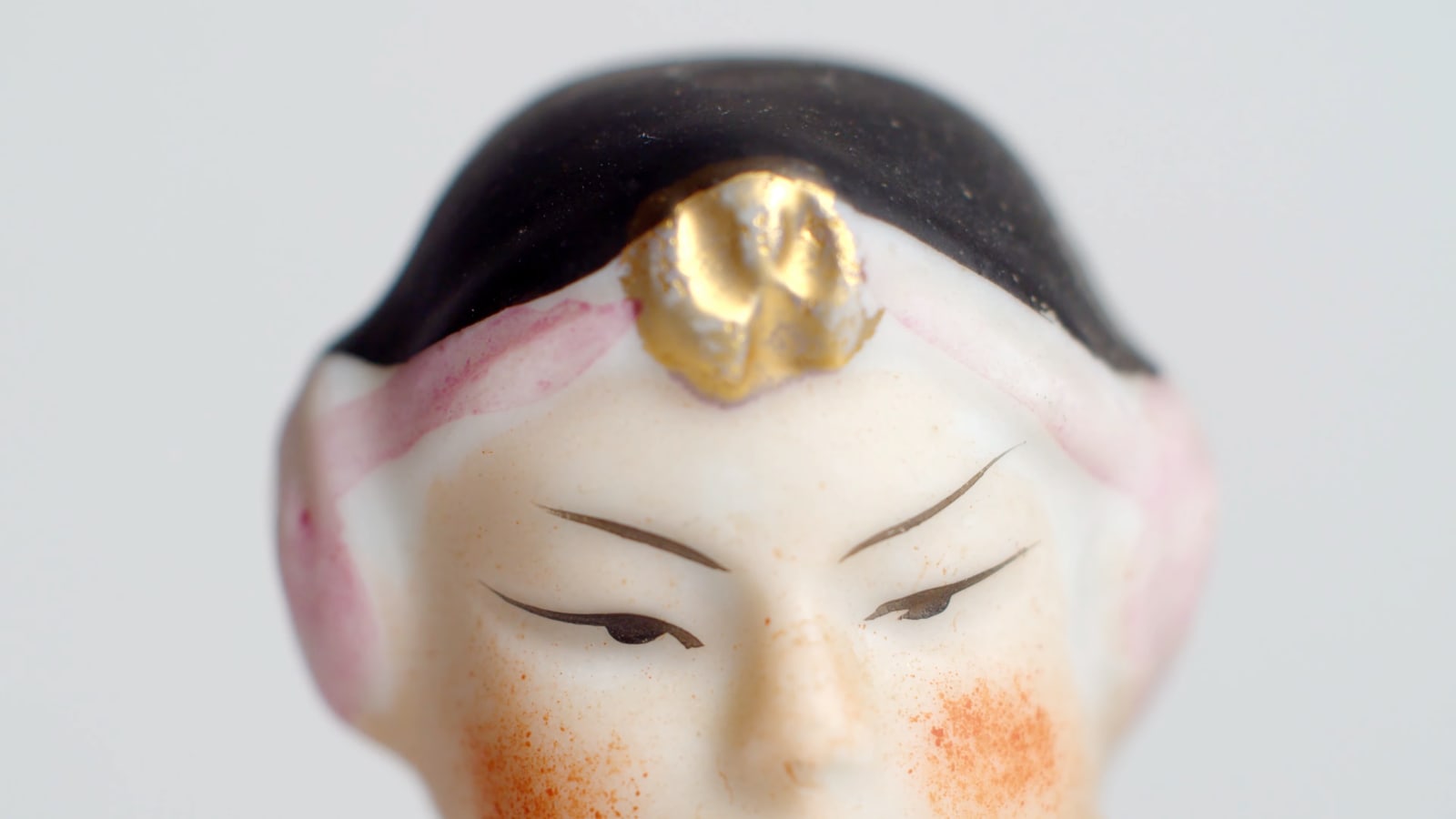 still from video shows top half of a painted figurine's face on white background
