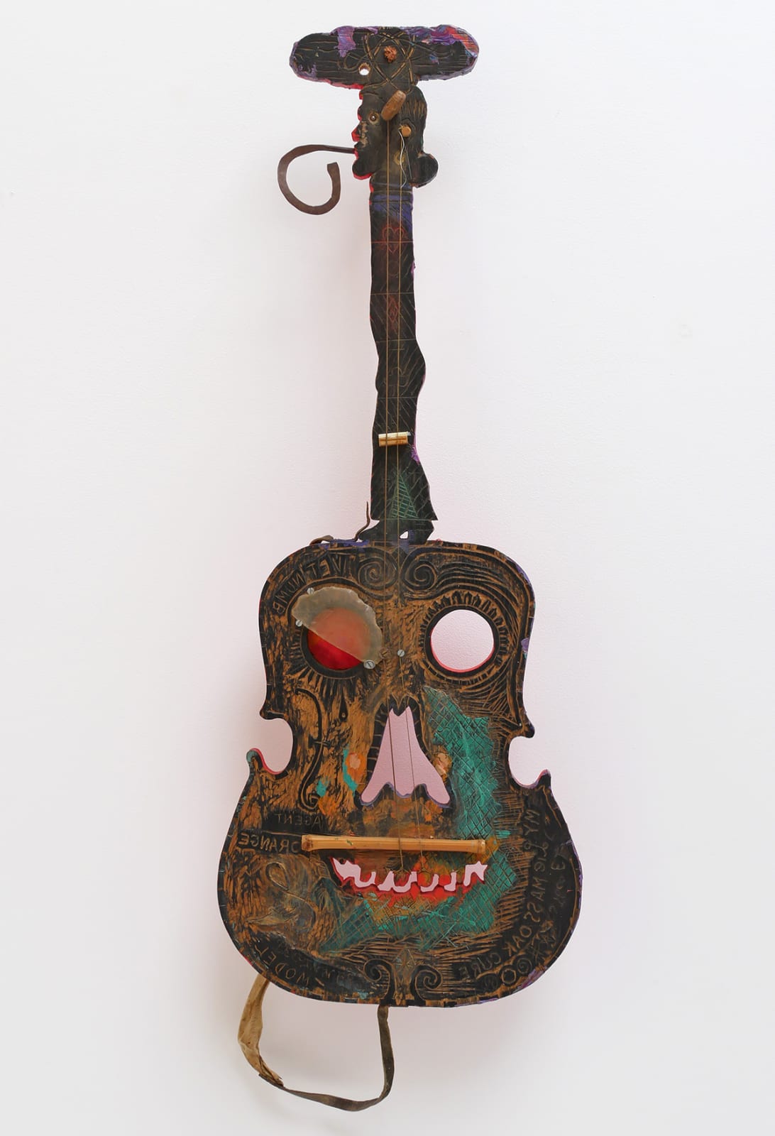 An image of a wooden guitar with a face with mixed media parts.