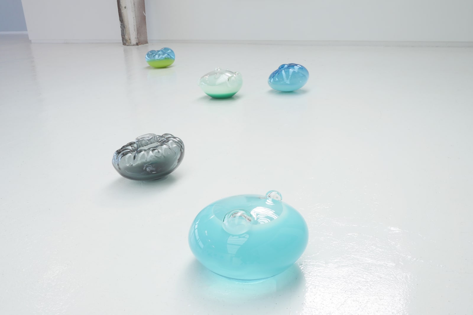 Five glass blown sculptures arranged on a white floor.