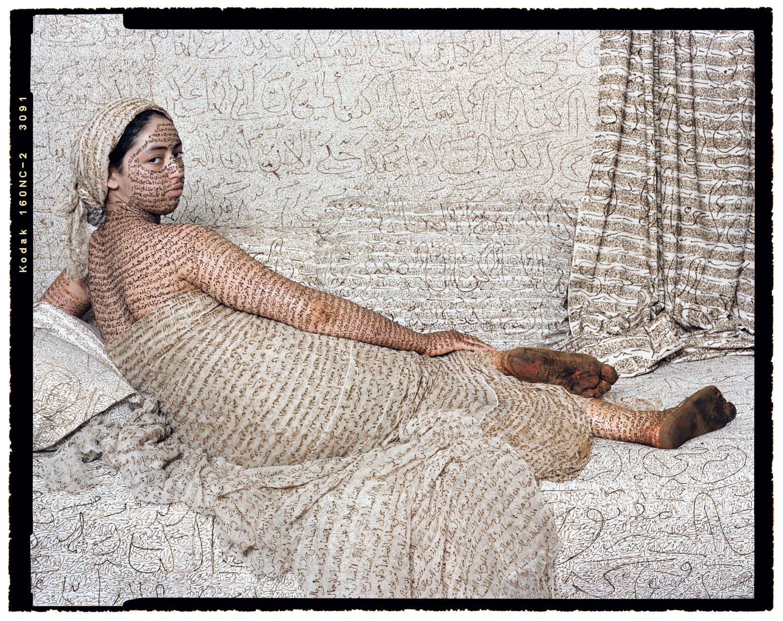 Lalla Essaydi Les Femmes du Maroc: La Grande Odalisque, woman posing to imitate subject in Jean Auguste Dominique Ingres' painting La Grande Odalisque, her skin and all fabric inscribed with Arabic calligraphy in henna