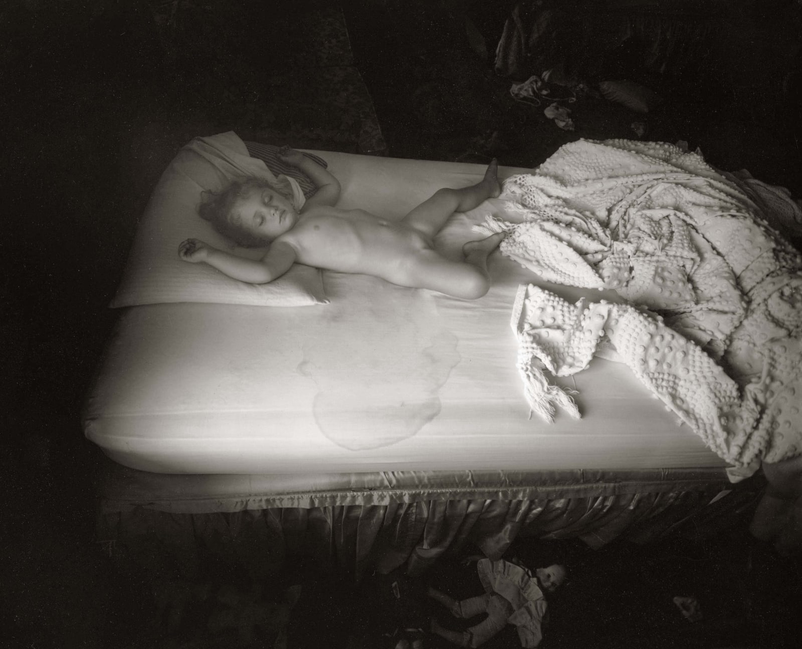 Virginia sleeping with wet bed stains and dolls on floor, from the Immediate Family series by Sally Mann