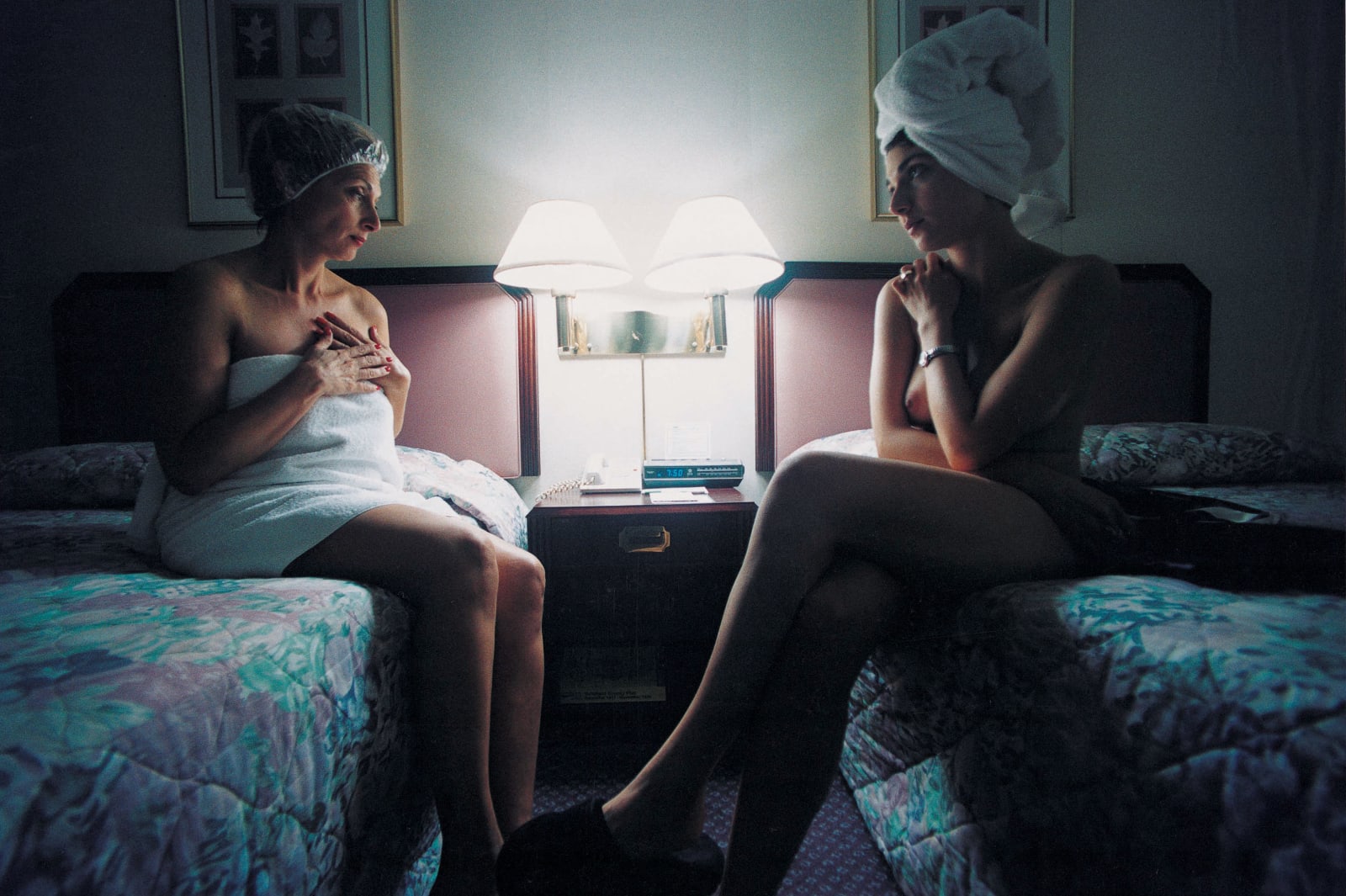Elinor Carucci My Mother and I in a Hotel Room mother in shower cap and towel seated on bed next to bed where nude artist sits with hair in towel