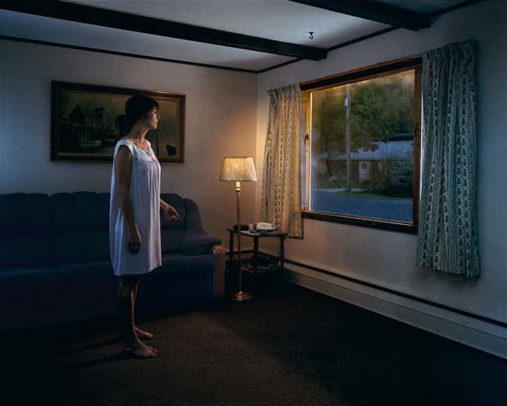 Woman in white nightdress looking out of window with circle drawn on glass pane by Gregory Crewdson