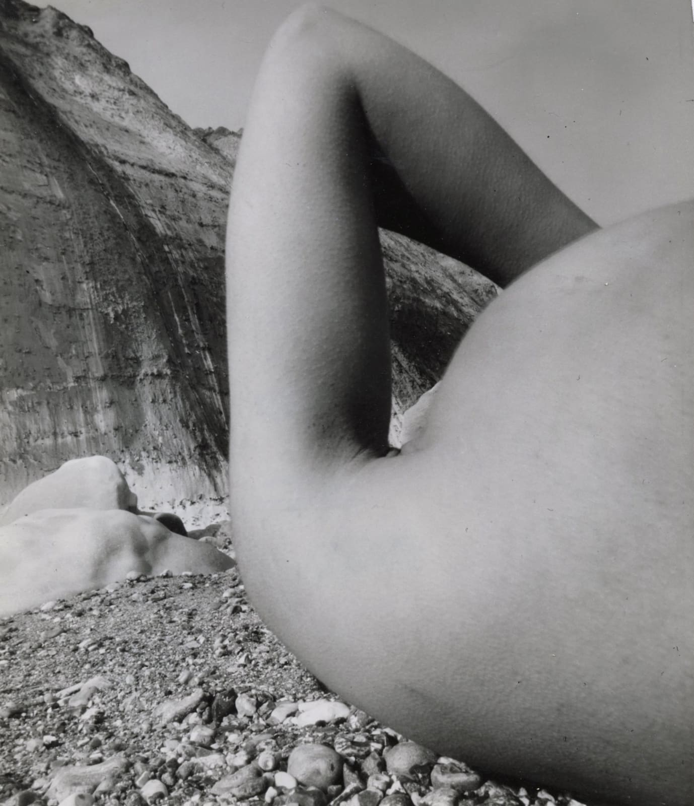 abstracted nude potrait of woman reclining on rocky beach with arm bent by BIll Brandt