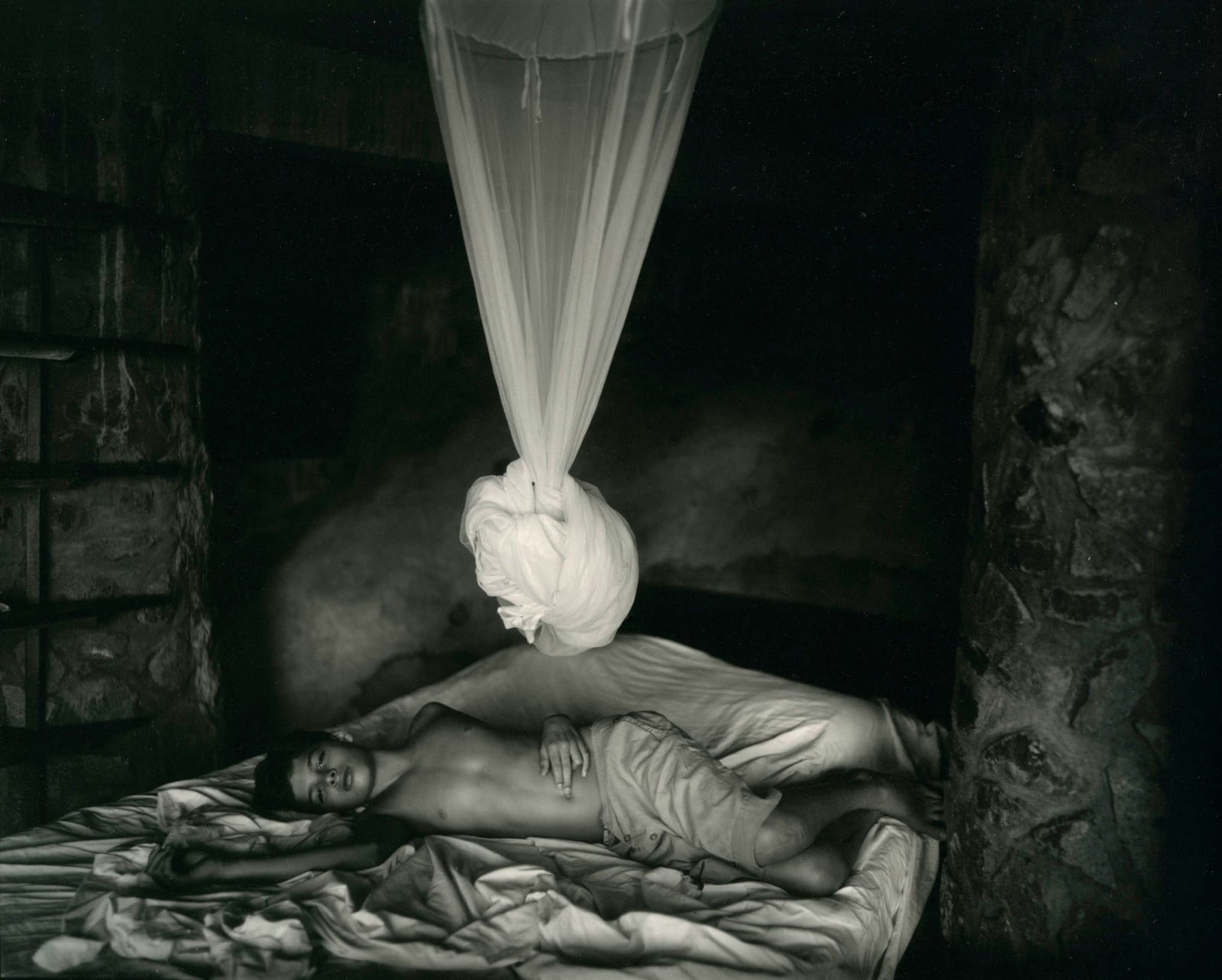 Sally Mann Immediate Family series, Sheet Changing Day, Emmett lying on bed with white bed canopy tied up above him