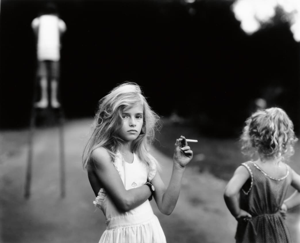 Virginia holding a candy cigarette, Virginia and Emmett in background, from the Immediate Family series, by Sally Mann