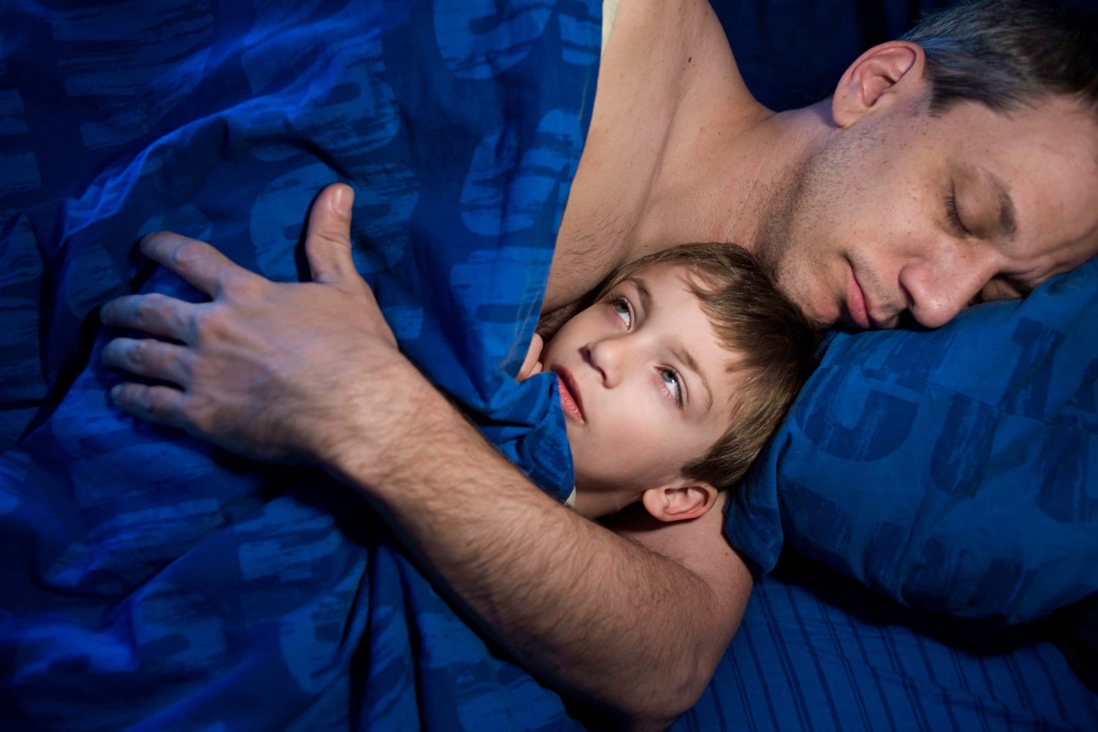 Elinor Carucci photograph of her husband and son sleeping with blue sheets