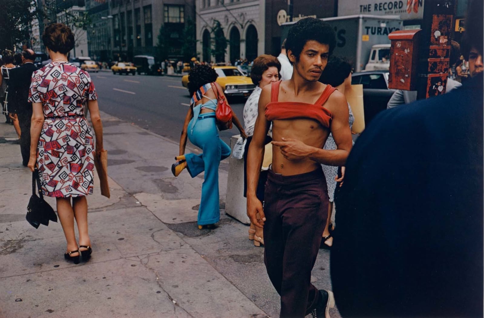 Man on New York City street with red tank top rolled up with other passersby taken by Joel Meyerowitz in the 1970s