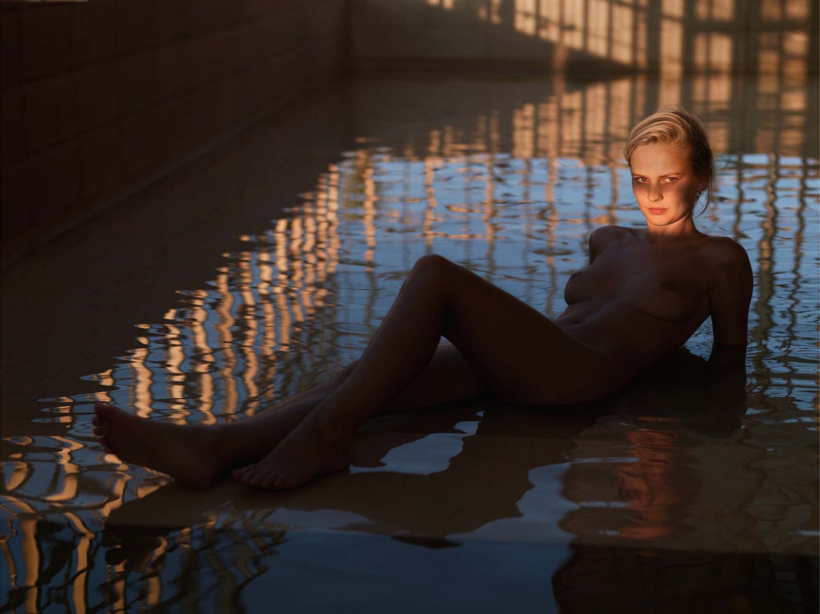 Mona Kuhn photograph of nude woman reclining in pool of water with only her head illuminated by the sun