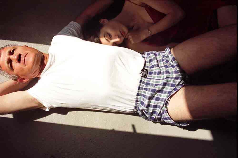 Elinor Carucci My Father and I #2 man in white shirt and boxer shorts lying in sunlight with woman lying next to him in shadow