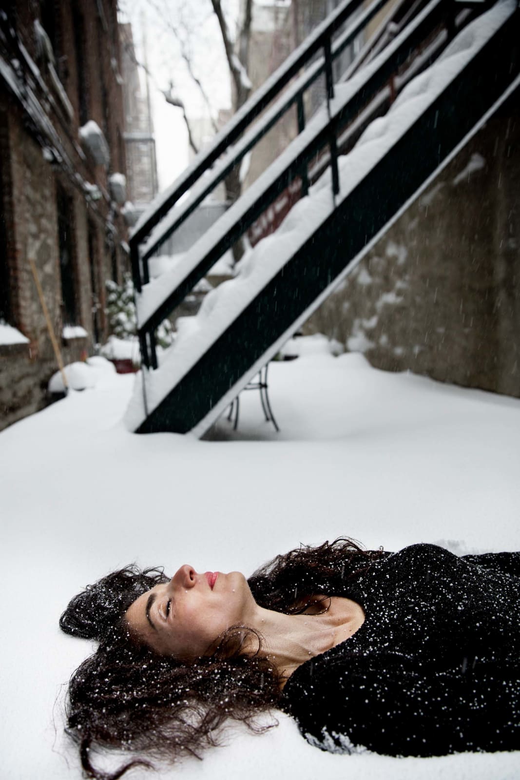 Elinor Carucci photograph of the artist laying in the snow in front of the stairs to an apartment building