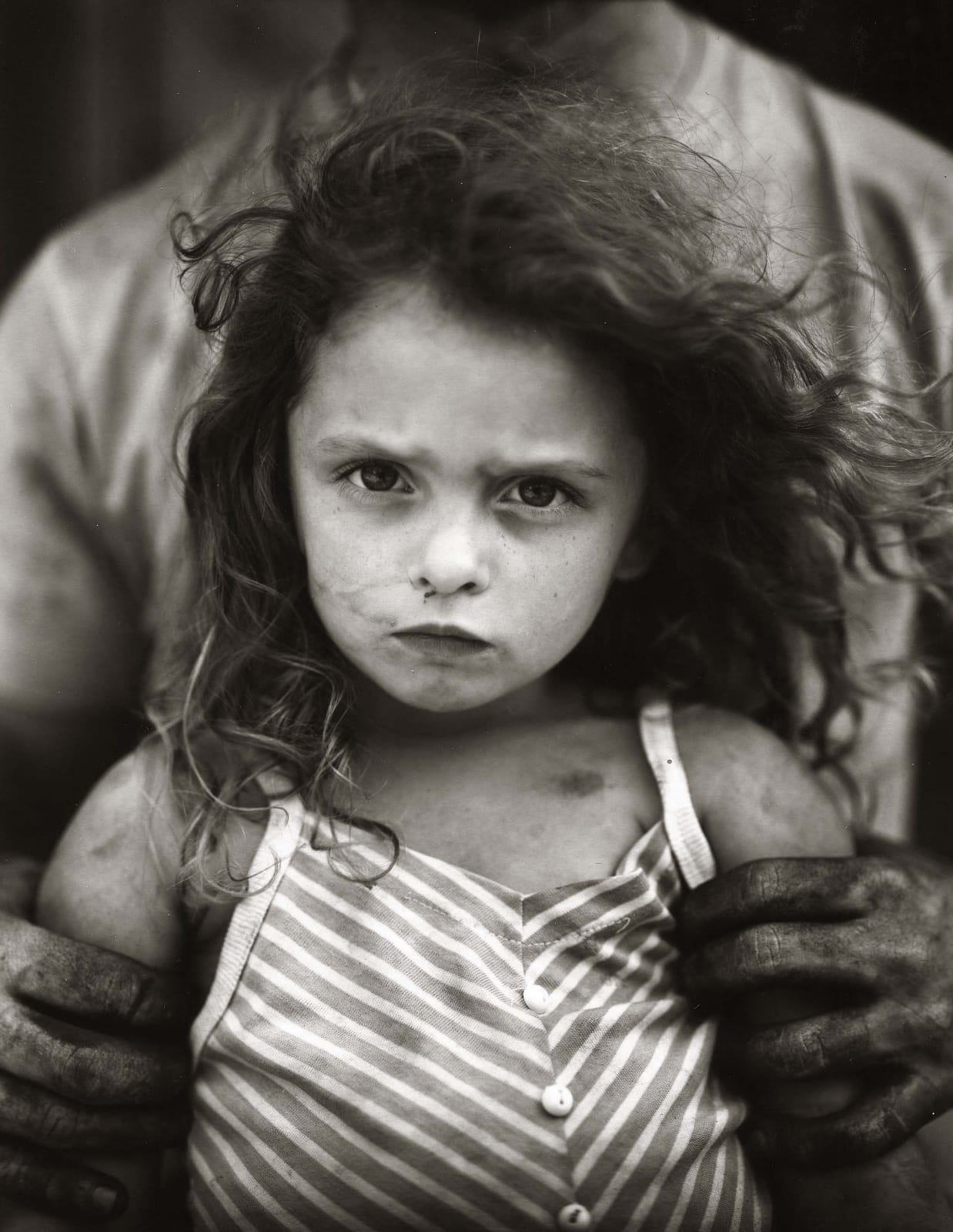 Larry holding daughter Virginia with oil slicked hands, from the Immediate Family series by Sally Mann