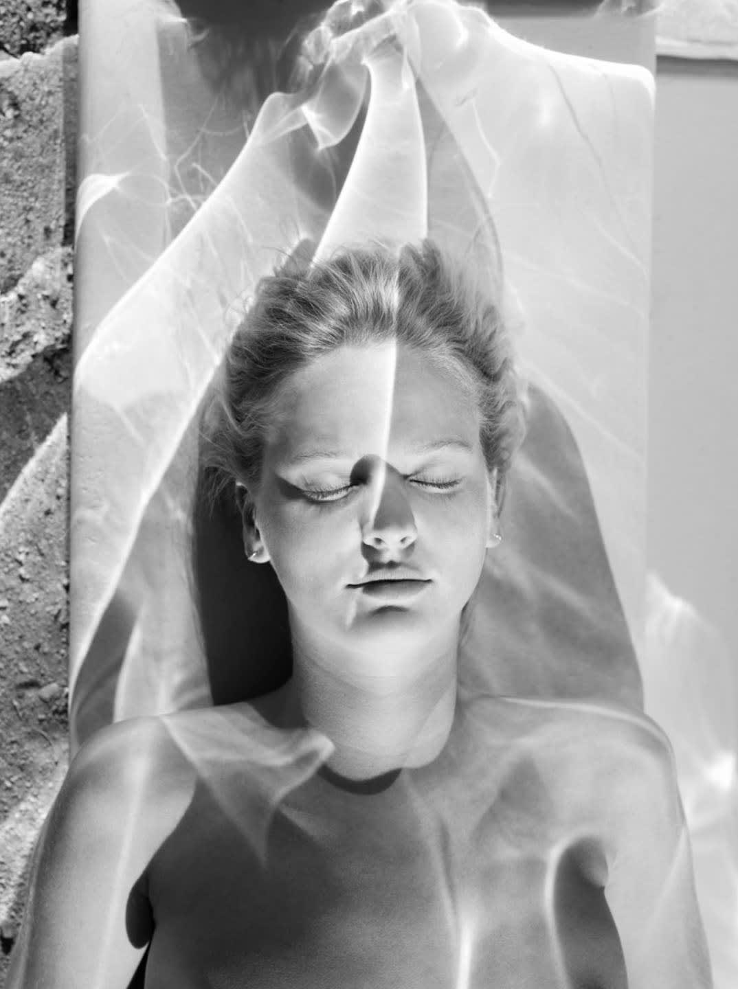 Mona Kuhn black and white photograph of woman lying down with eyes closed and refracted light shining on her body