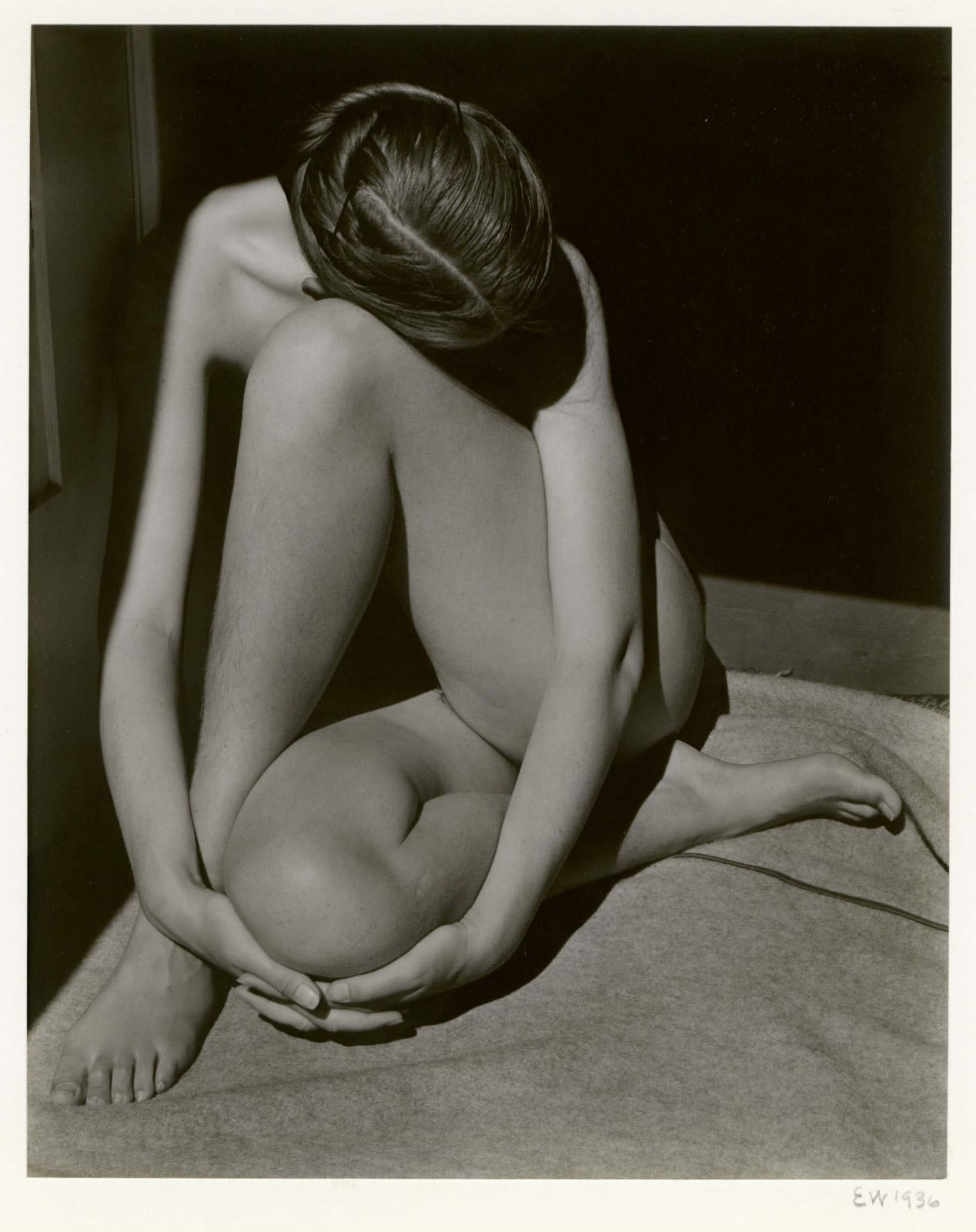 Edward Weston photograph of Charis Weston, nude, sitting in doorway with legs crossed and head resting on thigh