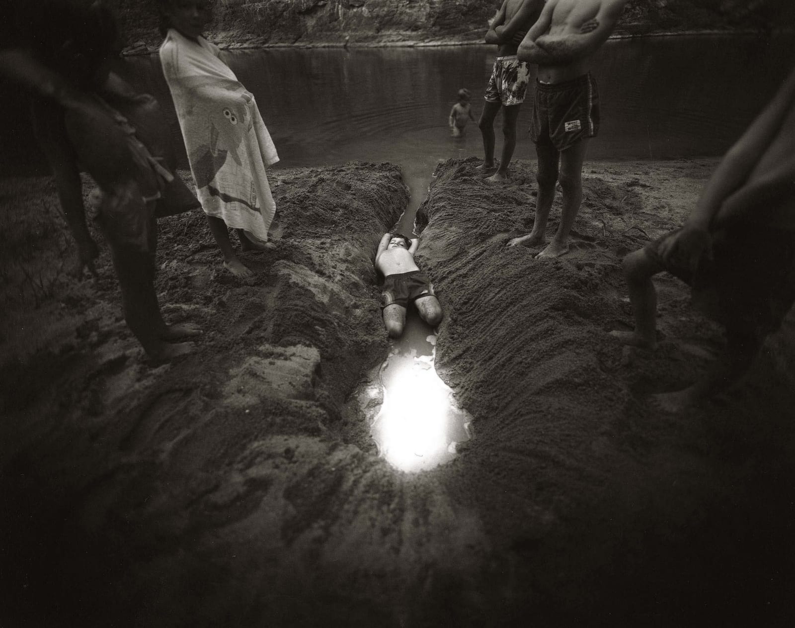 Emmett laying in a ditch filled with glowing water, from the Immediate Family series, by Sally Mann