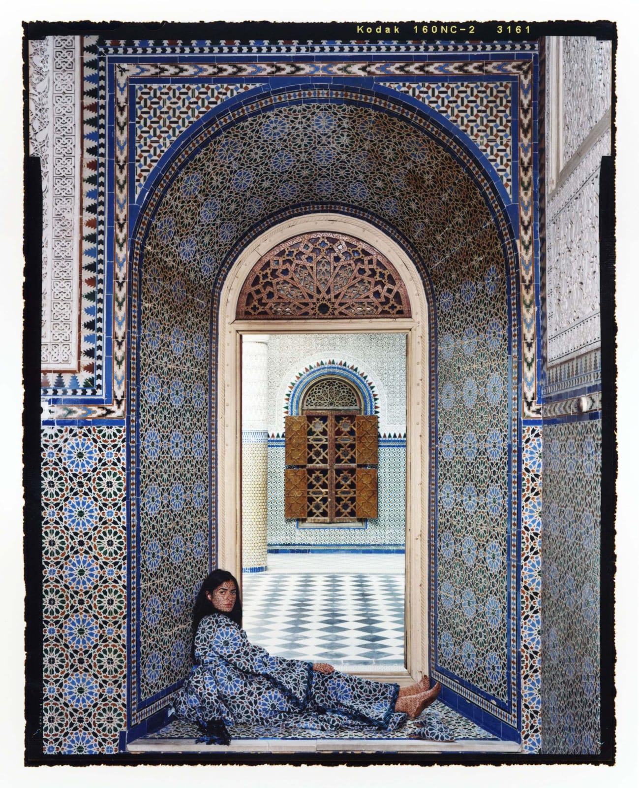 Woman sitting in doorway of Moroccan palace with blue tiles, by Lalla Essaydi