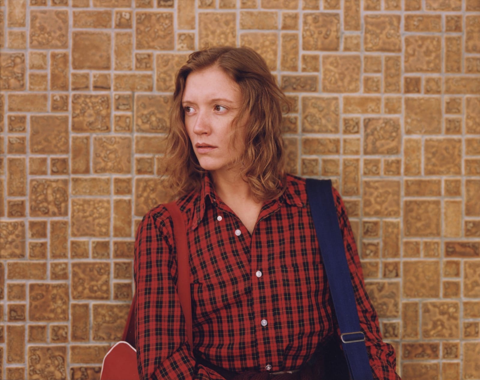 Ginger Shore wearing red plaid shirt against brick wall by Stephen Shore