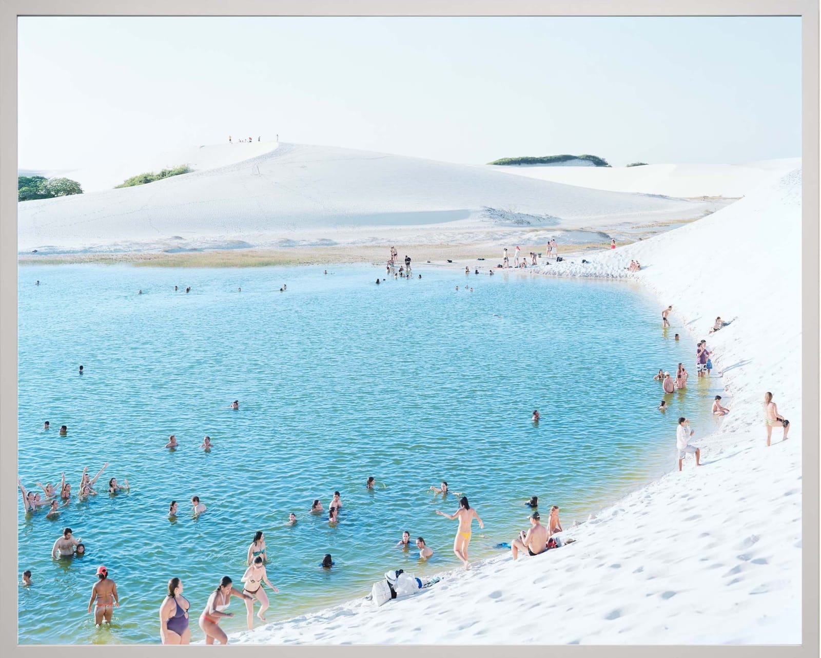 People swim and relax in a bright blue lagoon surrounded by white sand dunes; photograph by Massimo Vitali.