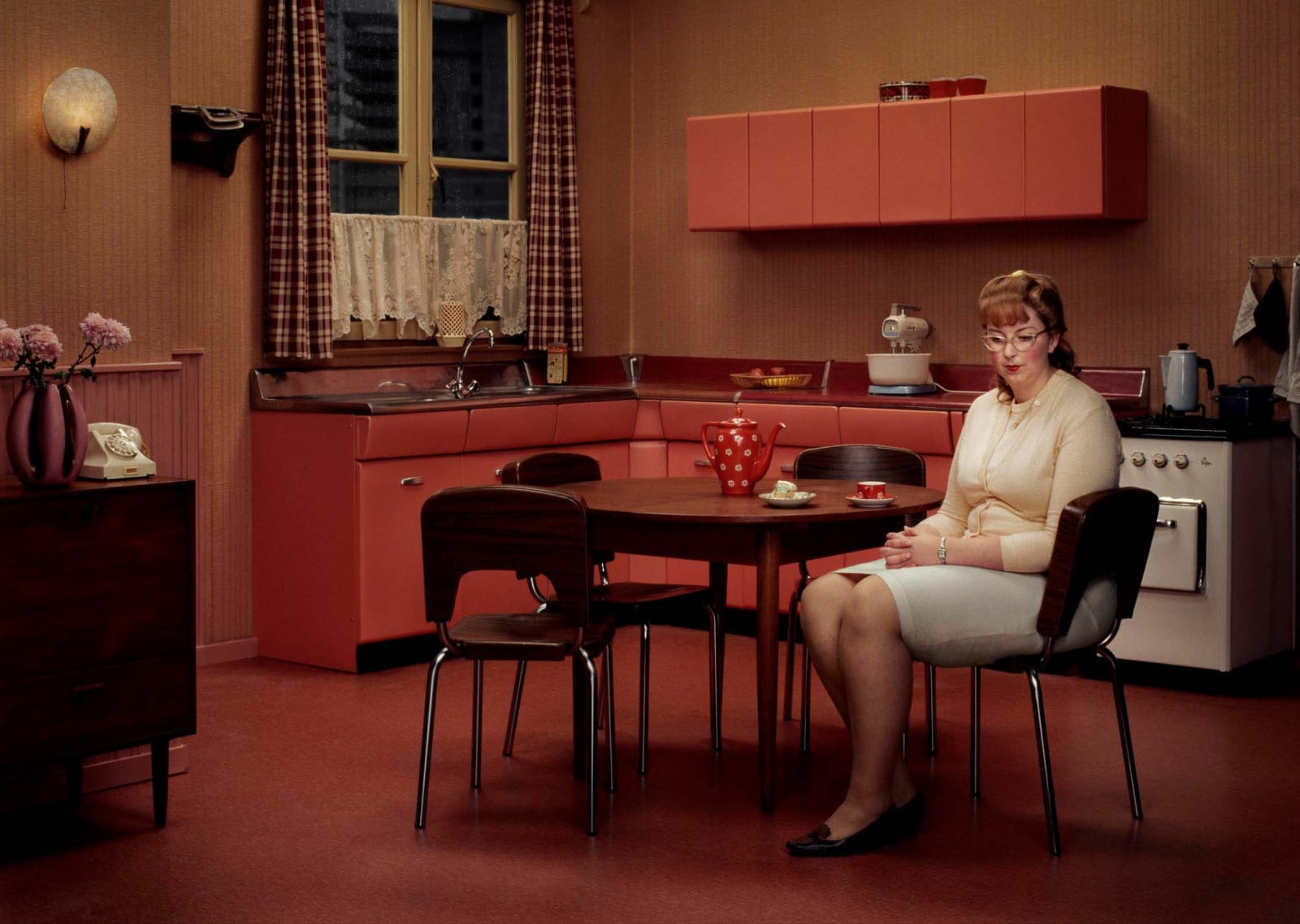 Erwin Olaf woman sitting in red midcentury kitchen with cake and tea on table