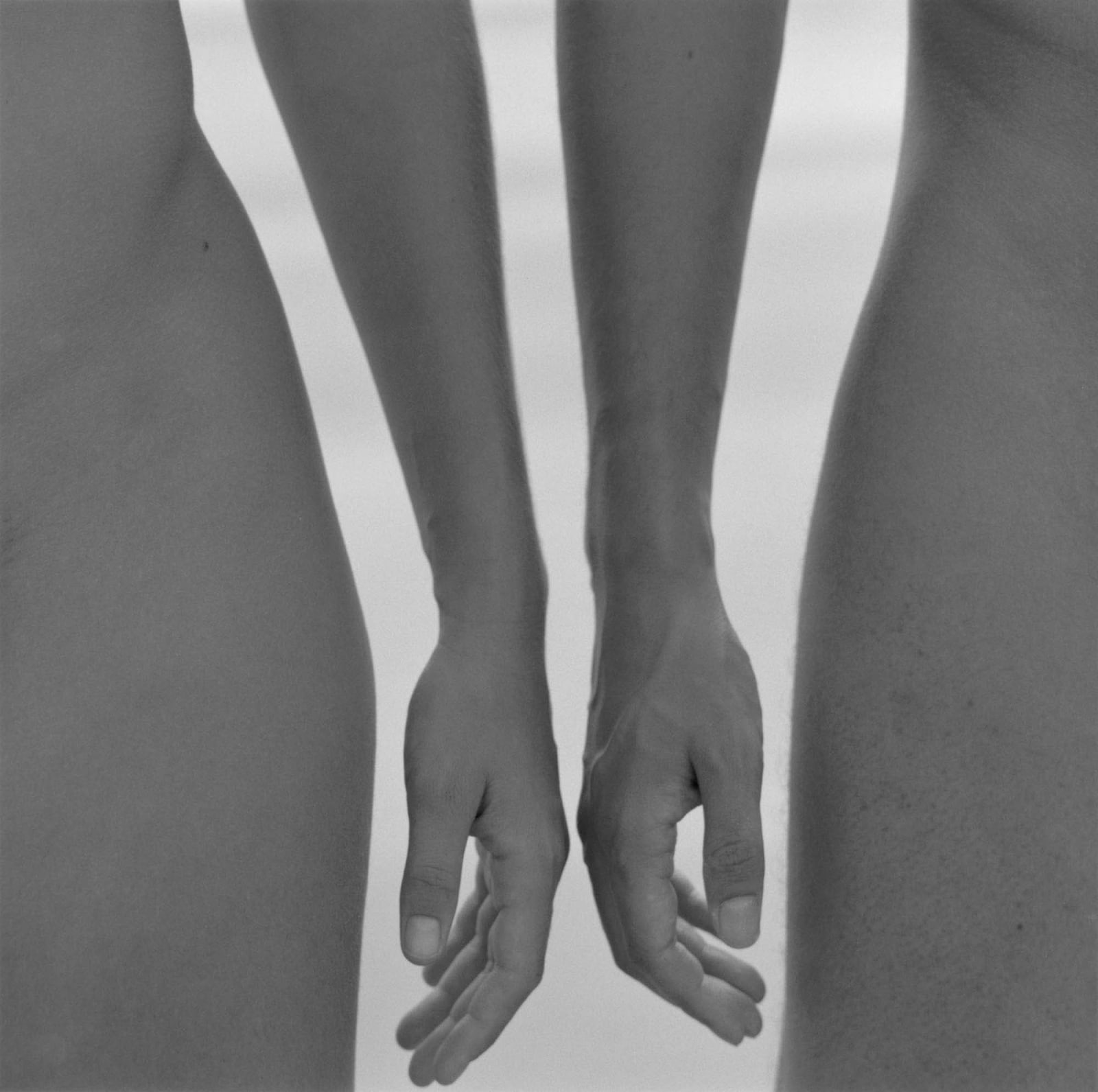 Mona Kuhn photograph of two arms and hands almost touching, framed by two hips