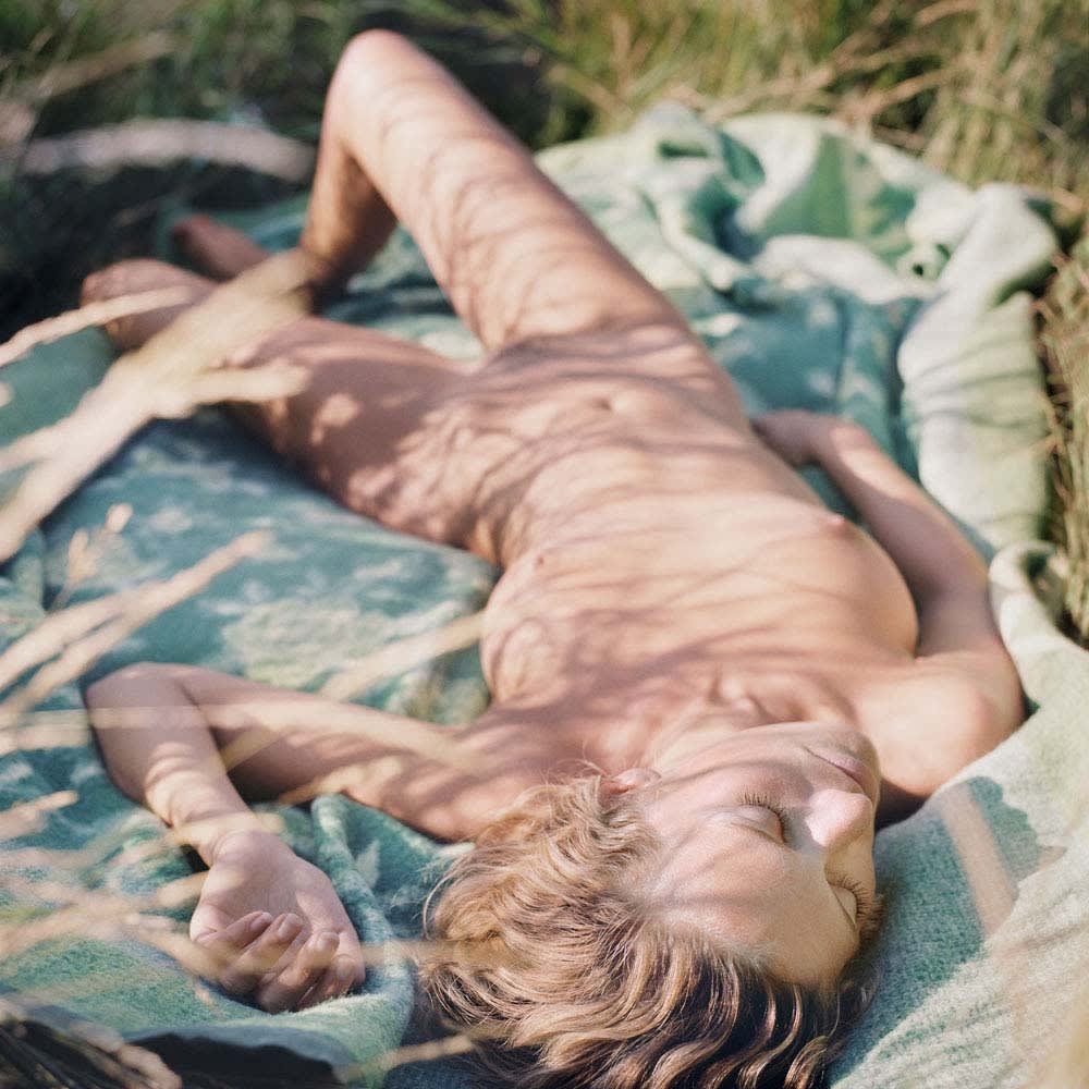 Mona Kuhn photograph of nude woman lying on blanket in grass with shadows of grass on her body