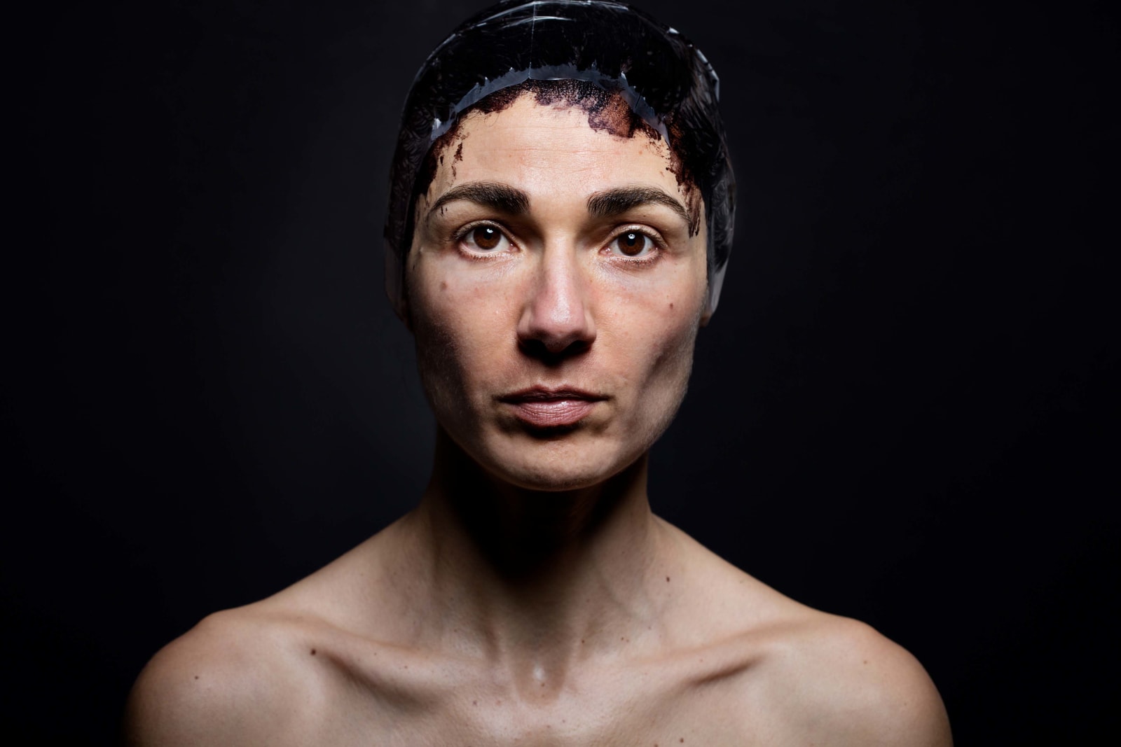 Elinor Carucci photograph portrait of the artist's face and shoulders against a black background with hair dye on her head