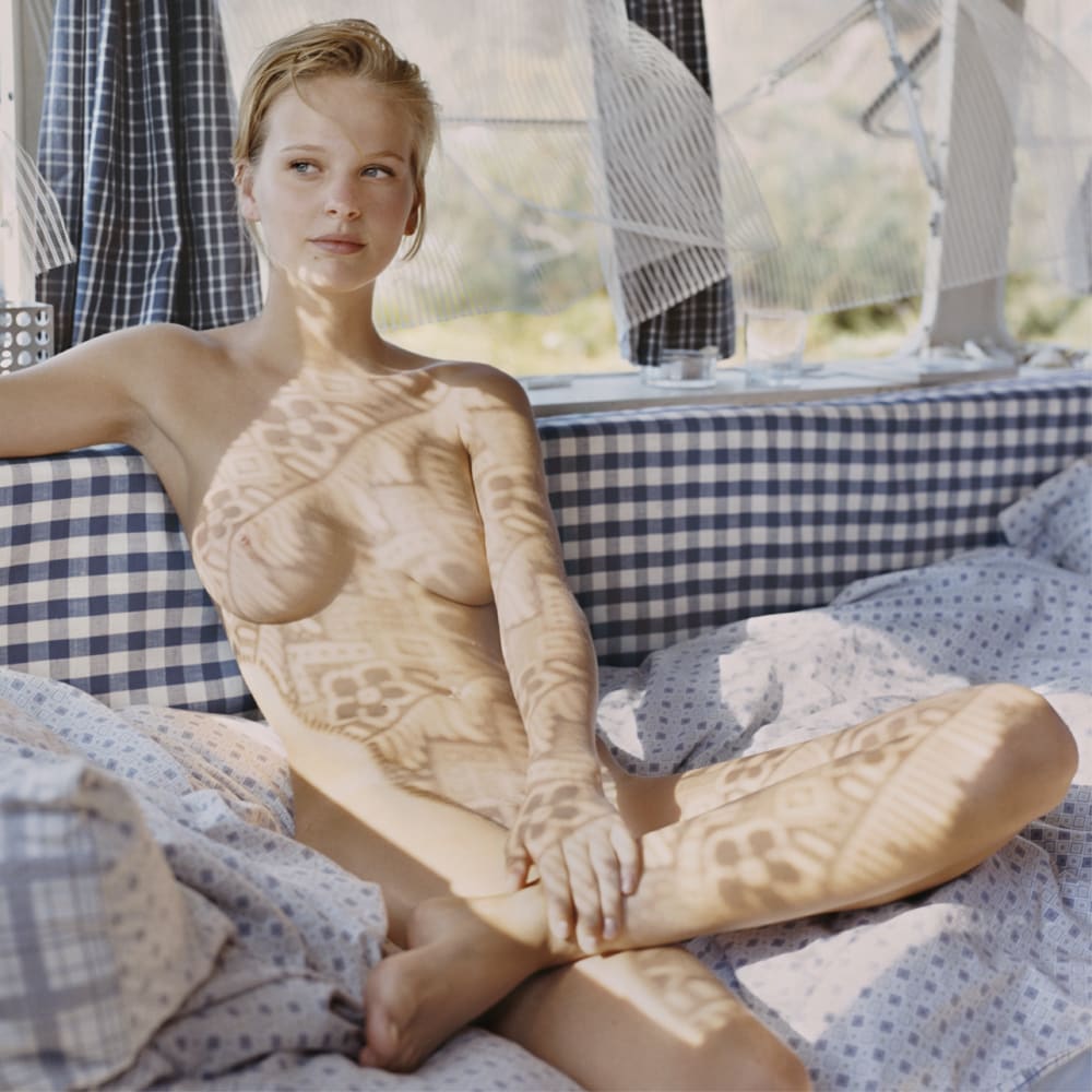 Lise sitting on blue couch, with curtain patterns shadowed onto her body, by Mona Kuhn