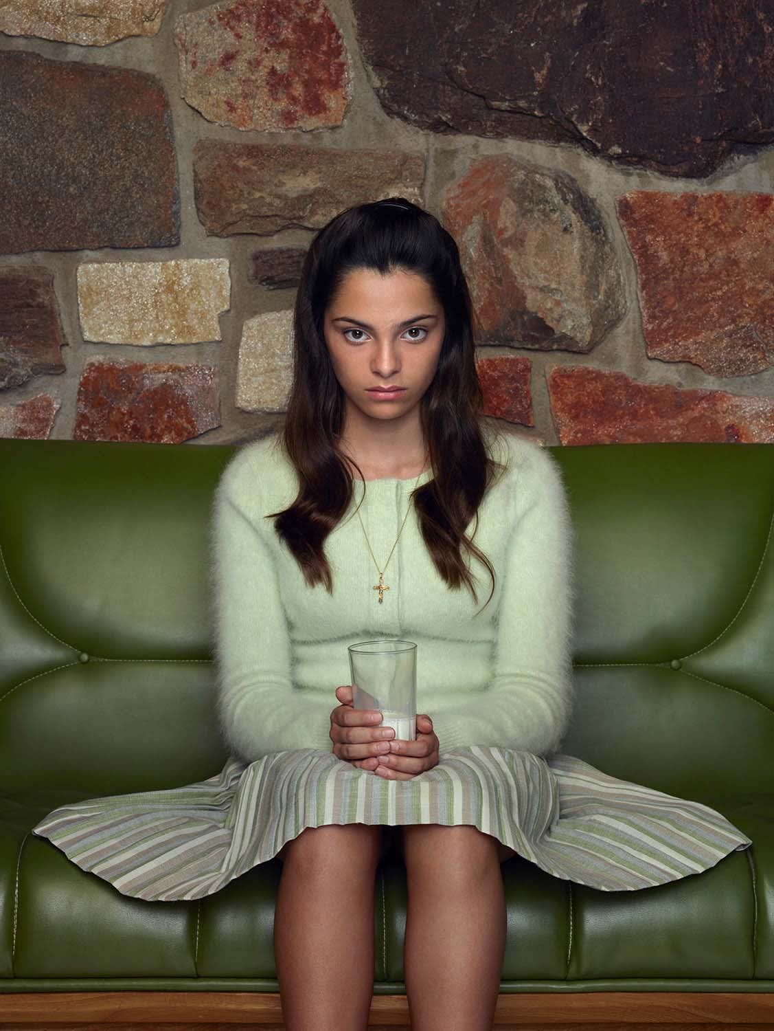 Young girl niece sitting on green couch, holding a glass of milk, from Palm Springs midcentury series, by Erwin Olaf