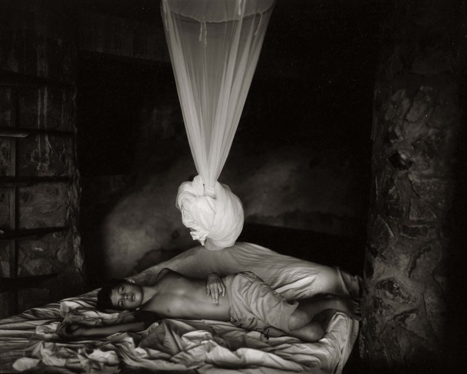Emmett lying on bed with mosquito ned tied above him, Sheet Changing Day, from Immediate Family series by Sally Mann