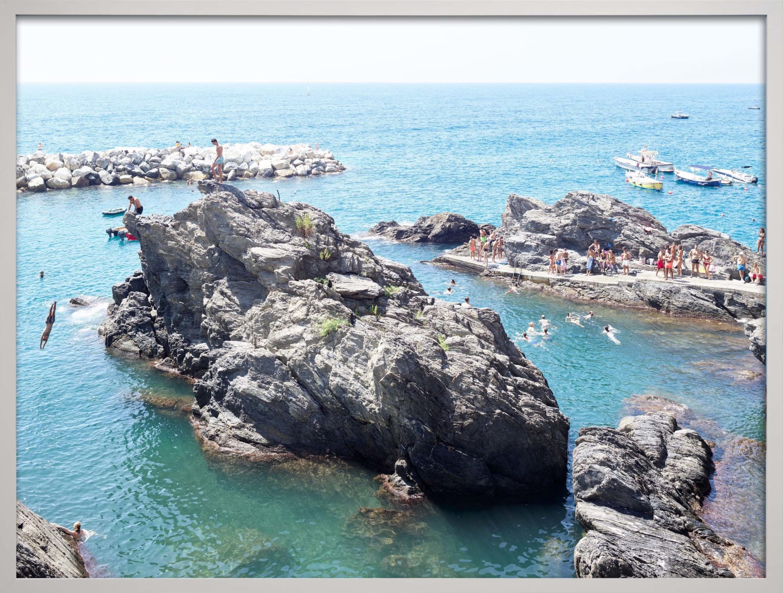 Beachgoers in water and boys diving off floating cliff, by Massimo Vitali