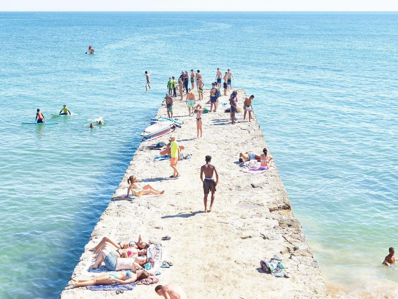 Carcavalos Pier in Portugal with people of all ages sunbathing and diving off pier into blue ocean, by Massimo Vitali