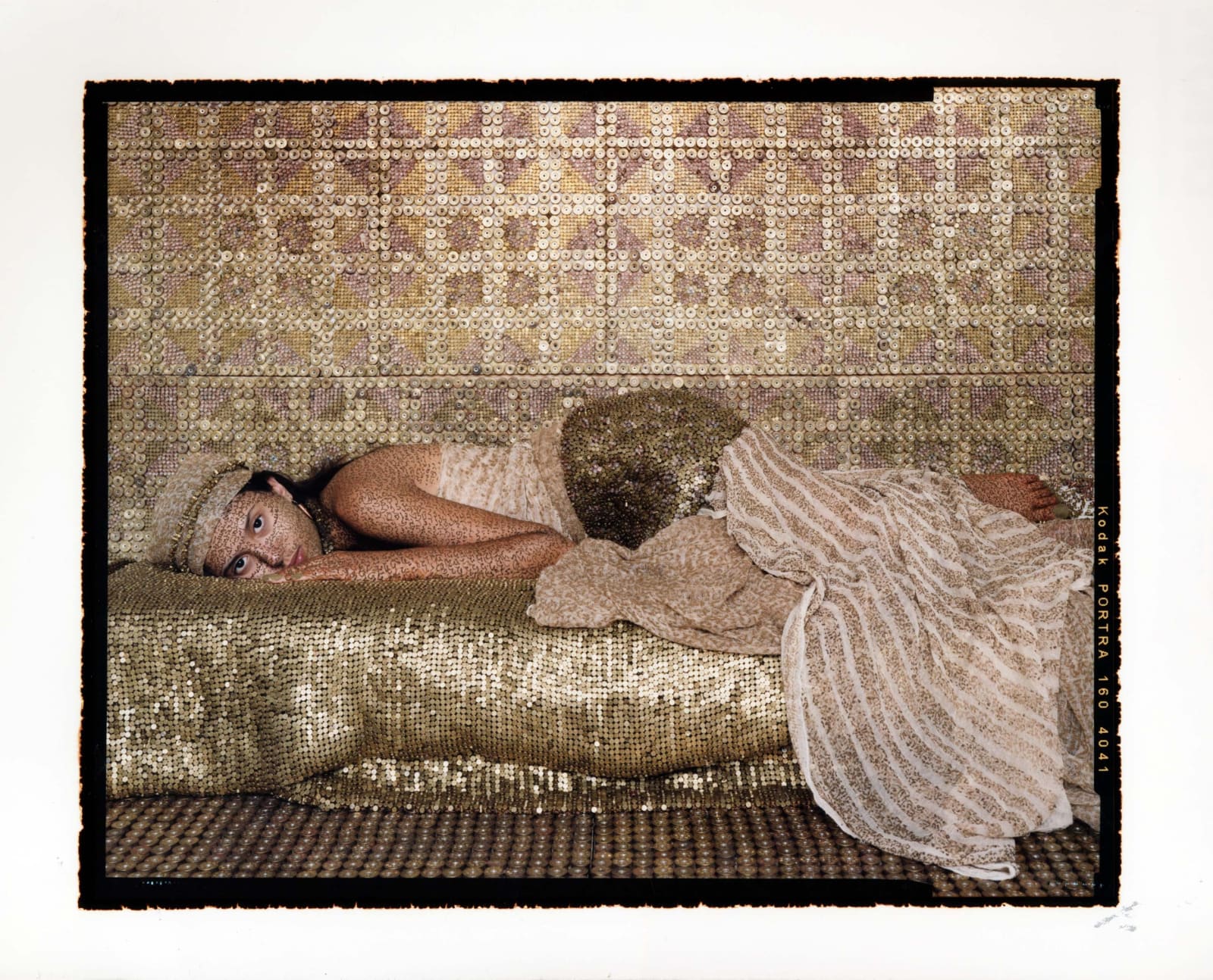 Woman lying on divan with fabrics made of golden bullets, by Lalla Essaydi