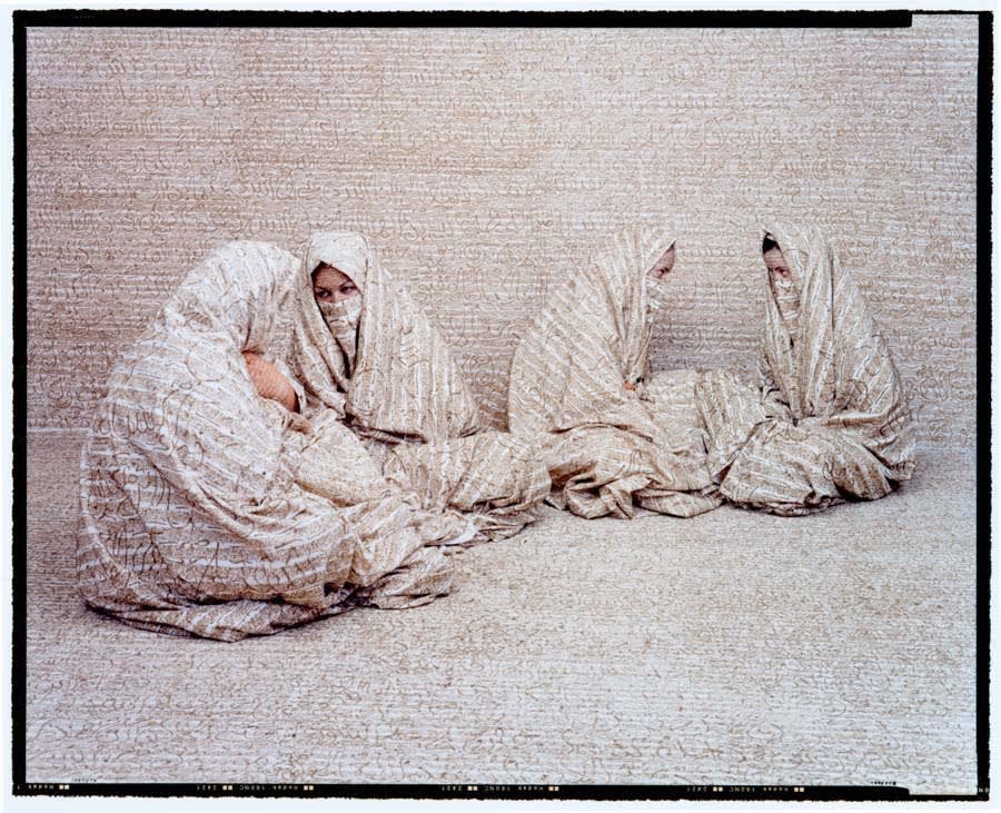 Four women sitting on ground in discussion, by Lalla Essaydi