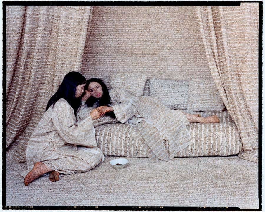 Two women in front of curtains wearing clothing inscribed with henna calligraphy, by Lalla Essaydi