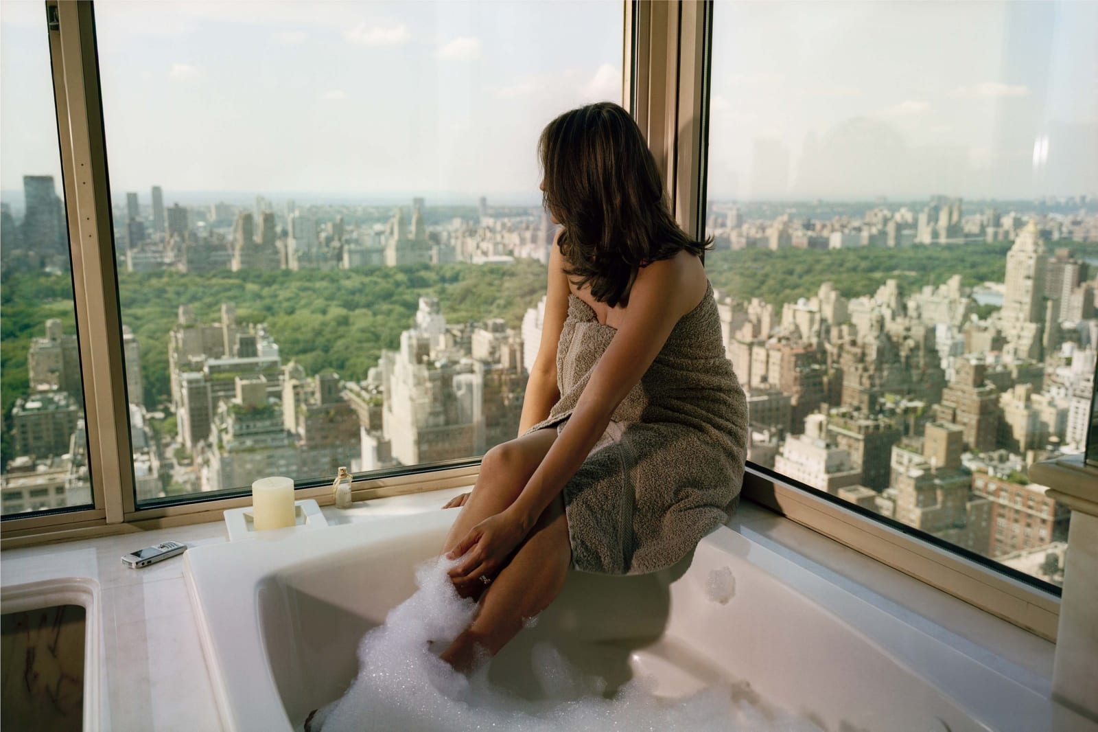 Gail Albert Halaban Out My Window New York Out My Window, Upper East Side, Bubbles, 2007 brunette woman in towel in bubble bath looking out corner window at Central Park and skyline