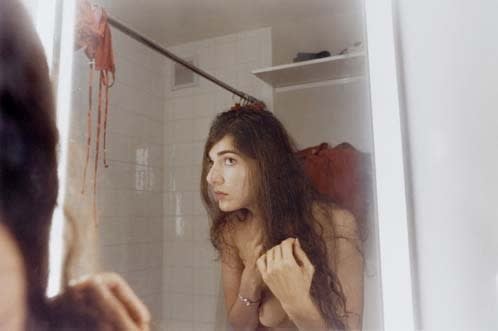 Elinor Carucci First Gray Hair woman examining her hair in bathroom mirror