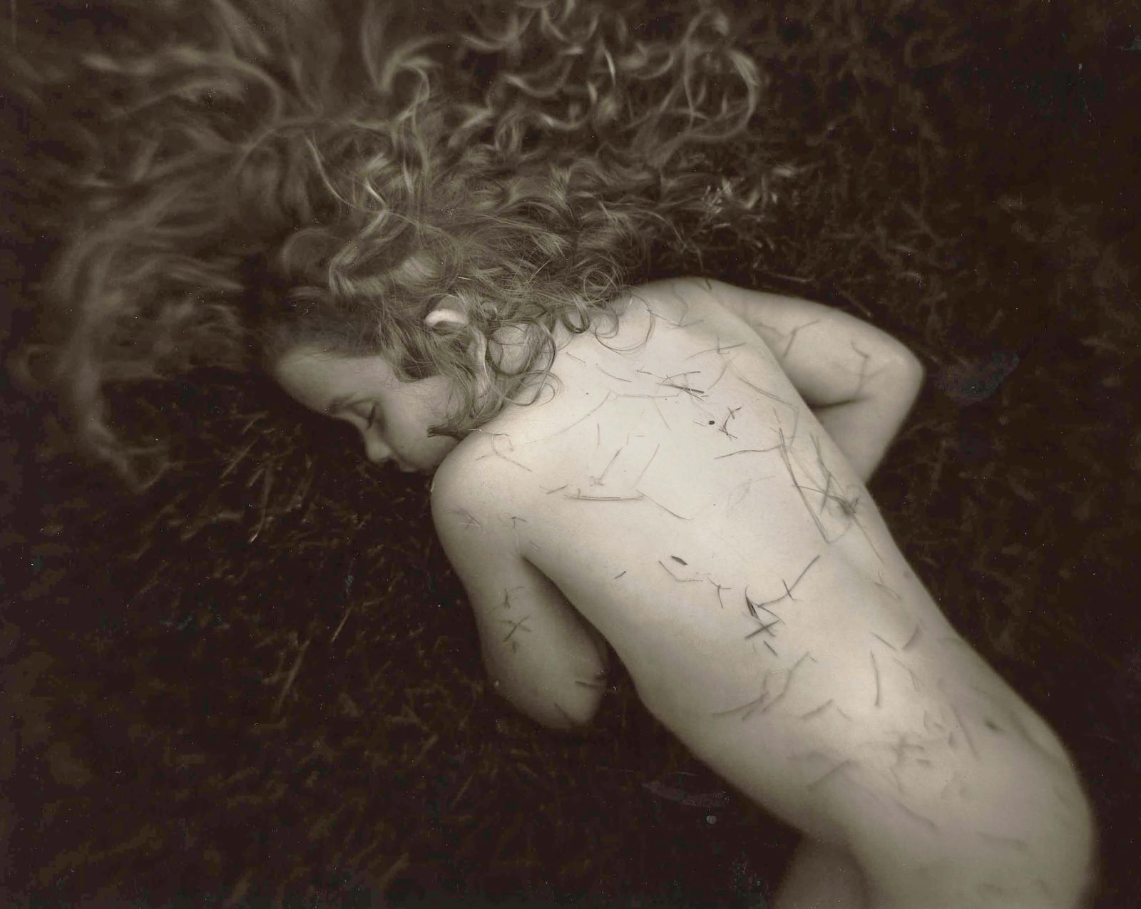Sally Mann Immediate Family series, Fallen Child, Virginia lying down on grass with blades of grass on her skin