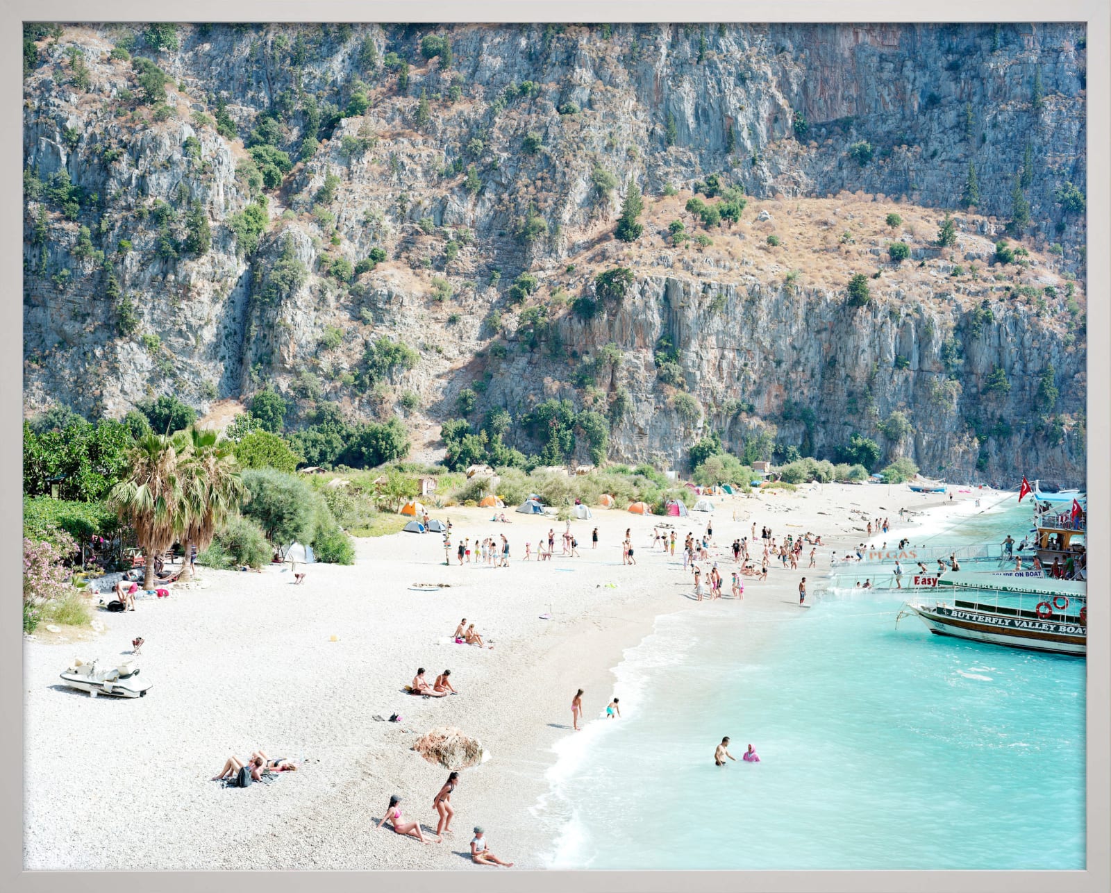 Beachgoers relaxing by the ocean with cliffs in background in Butterfly Valley, Turkey, by Massimo Vitali
