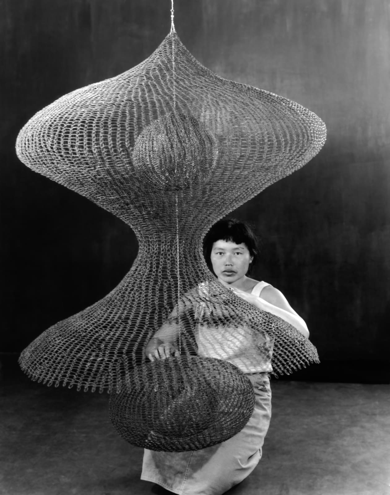 Imogen Cunningham, Ruth Asawa Kneeling Behind a Hanging Looped-Wire Sculpture, 1957