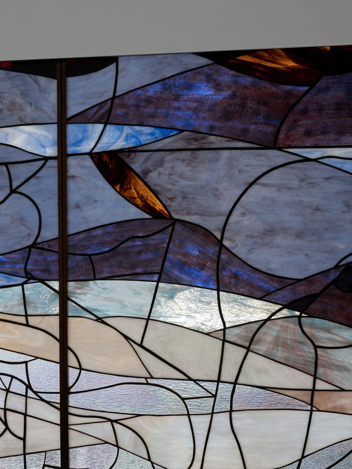 Room with a dark blue, green and orange stained glass window made up of 3 panels against a plain wall Rindon Johnson Clattering, 2021 Stained glass work (3 panels) and ash wood bench Glass work: 360 x 158 cm 141 3/4 x 62 1/4 inches Bench: 200 x 49 x 80 cm 78 3/4 x 19 1/4 x 31 1/2 inches
