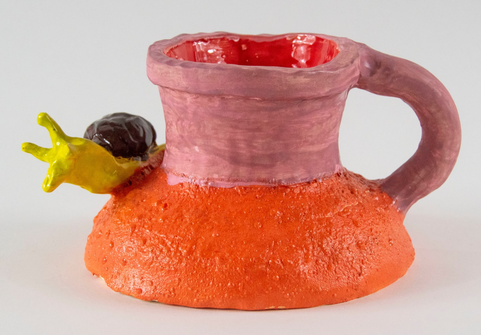 A red and orange cup with a large handle. There is a yellow snail sitting on the cup. By artist Reniel Del Rosario.