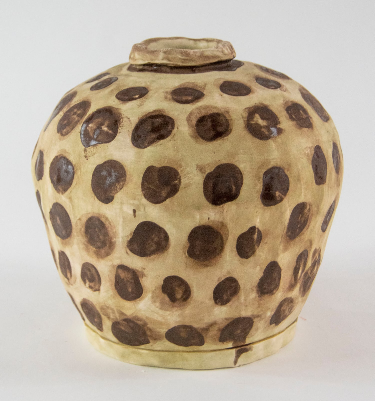 A yellow vase decorated with many brown circles by artist Reniel Del Rosario