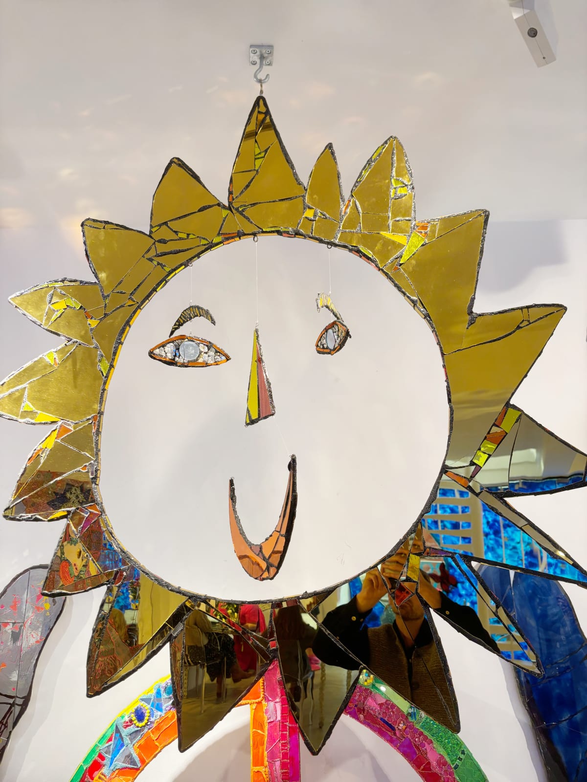 Large mixed media artwork, by British sculptor Andrew Logan. A gold mirrored sun shape expressing a smile, creating a joyful impression.