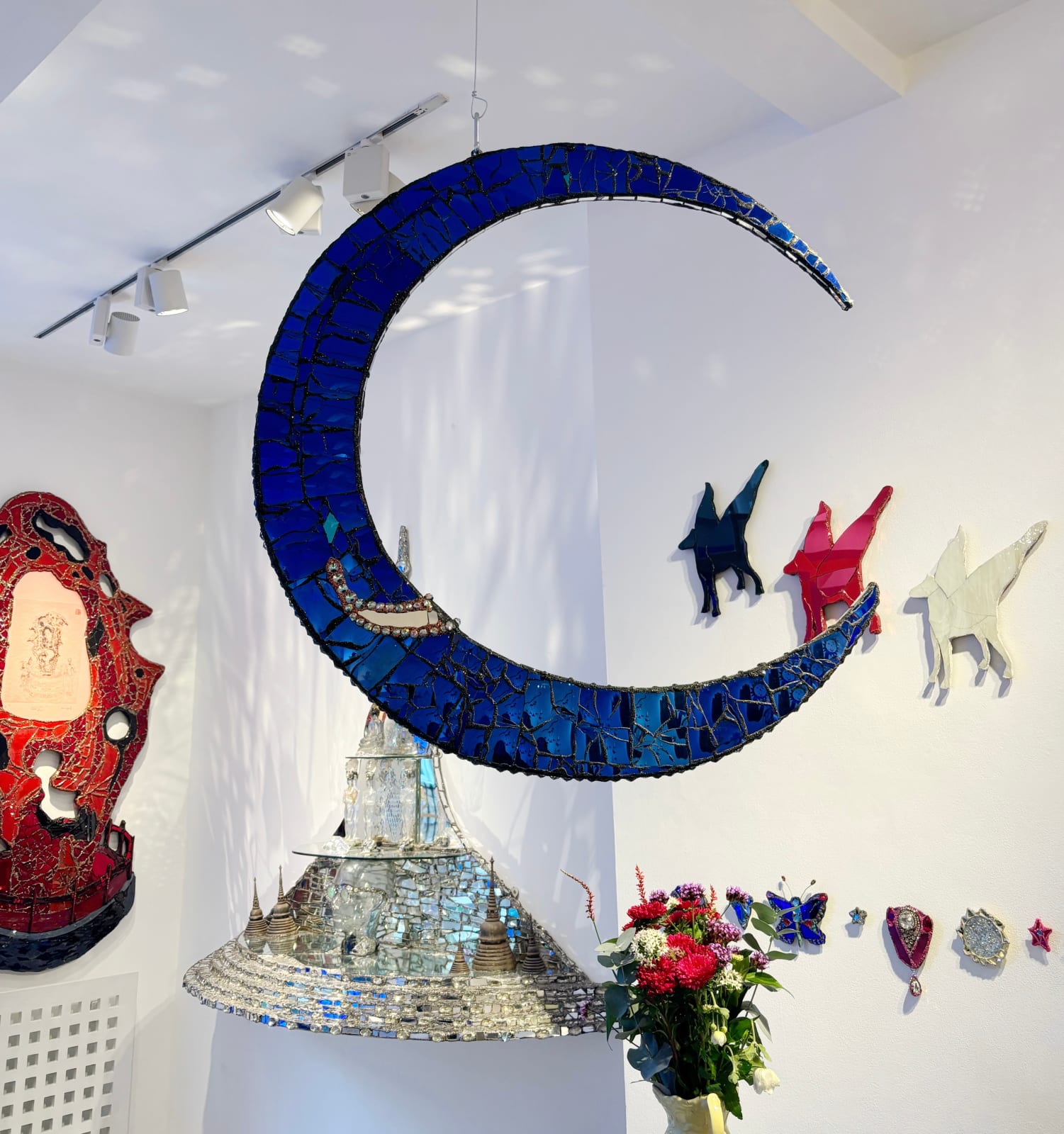 Vibrant mixed media artwork by British sculptor Andrew Logan. A mirrored dark blue crescent suspended for a radiant shimmering impression of the moon.