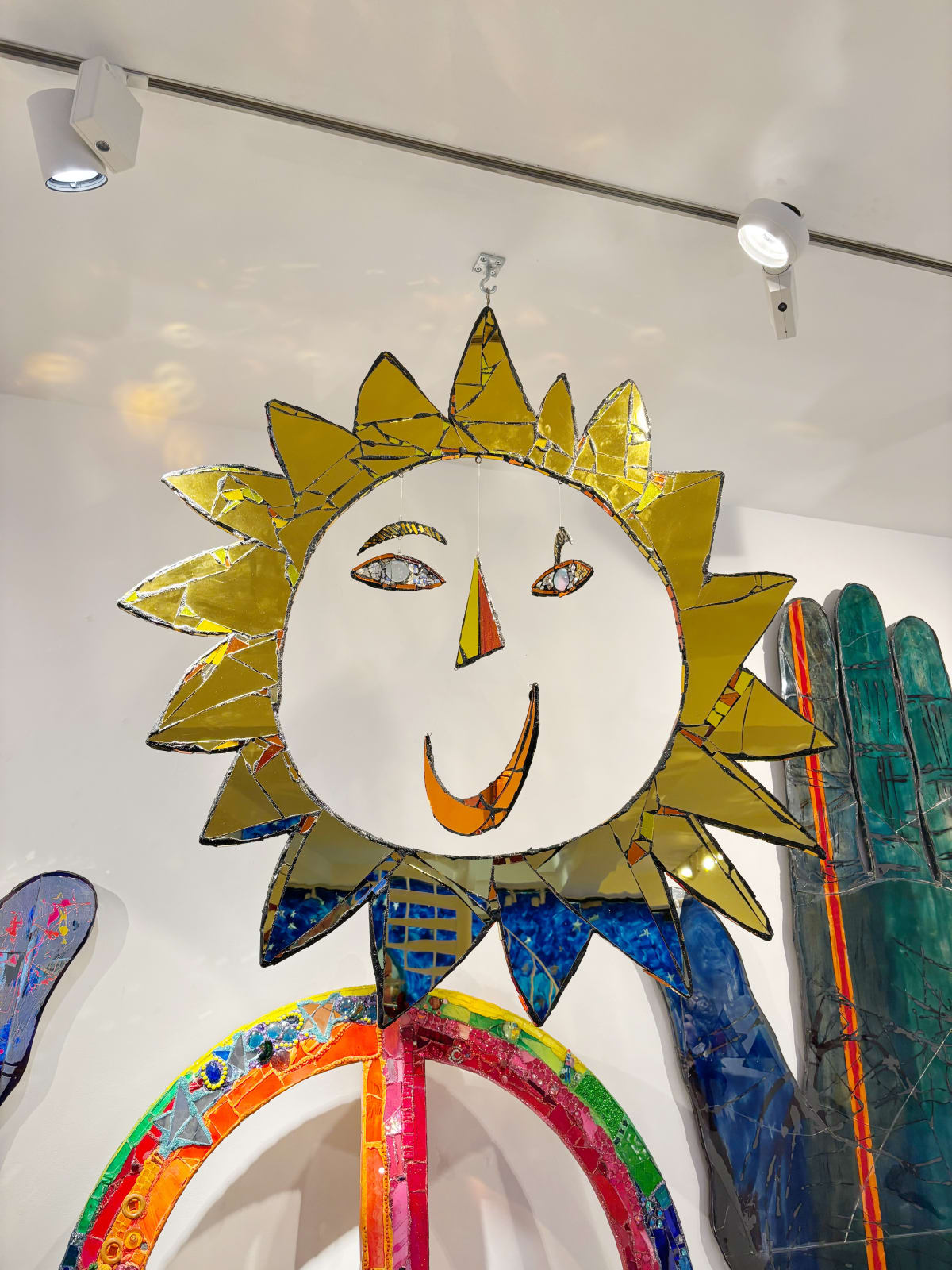 Large mixed media artwork, by British sculptor Andrew Logan. A gold mirrored sun shape expressing a smile, creating a joyful impression.