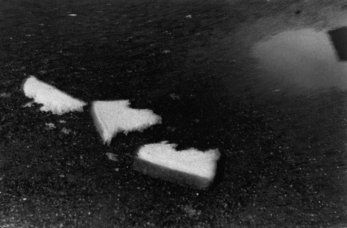 Mark Cohen, Three pieces of bread near a puddle, January, 1975