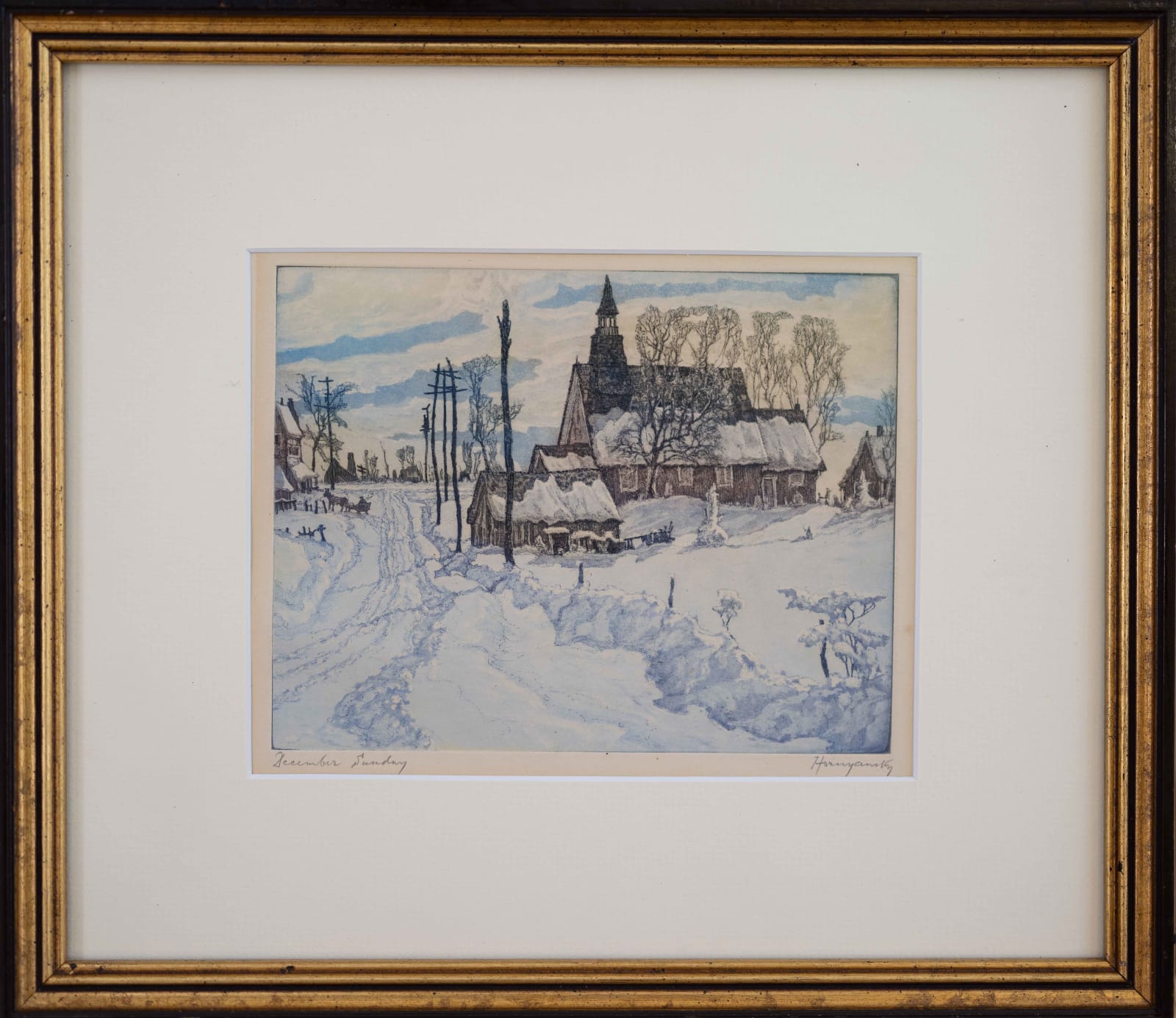 Framed photo of A snow-covered road takes the viewer into the composition, leading to a church or chapel with a prominent spire, which is a central feature of the image.