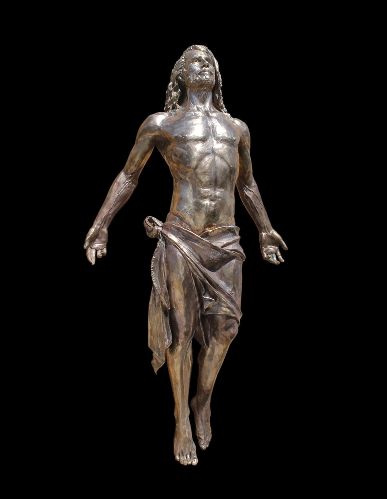Bronze statue of Jesus ascending, depicted with outstretched arms and upward gaze. His muscular figure is draped with a flowing cloth around his waist, conveying movement and spiritual elevation. The background is white, emphasizing the sculpture's detailed craftsmanship.