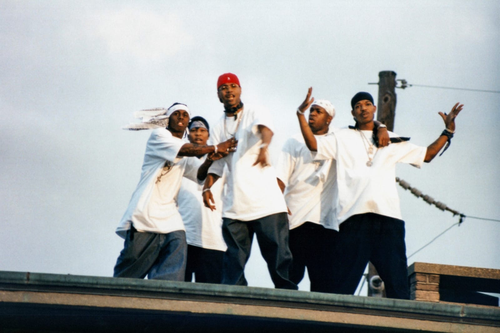 A photo by Polo Silk of the Hot Boys rap group featuring Lil Wayne, Mannie Fresh, Juvenile, Baby, and BG. The five are up on a roof with a white sky behind them, all wearing white t-shirts.